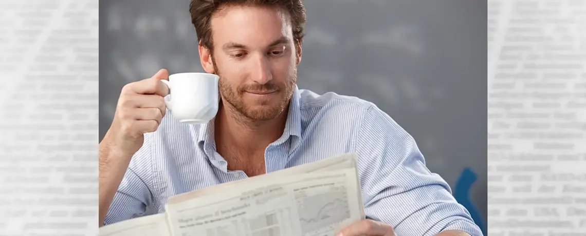 Mann trinkt einen Kaffee und liest die gedruckte Zeitung