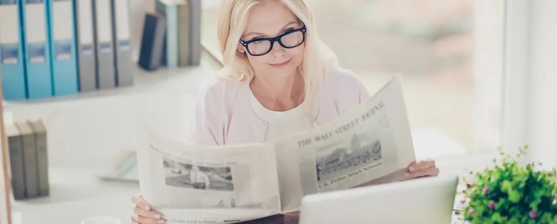 Eine Frau sitzt am Schreibtisch und liest die gedruckte Zeitung