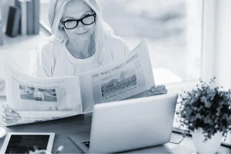 Eine Frau sitzt am Schreibtisch und liest die gedruckte Zeitung