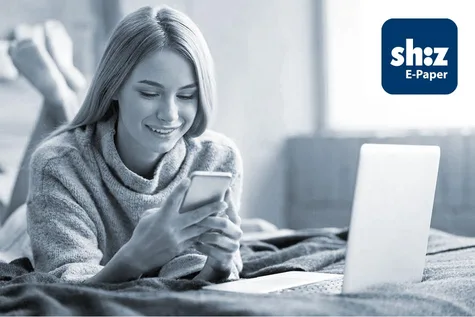 Junge Frau liegt auf einem Bett und liest auf ihrem Smartphone die digitale Zeitung in der App shz E-Paper