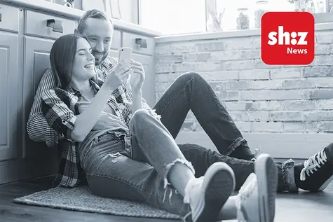 Junges Pärchen sitzt auf dem Boden und liest auf dem Smartphone die App shz News