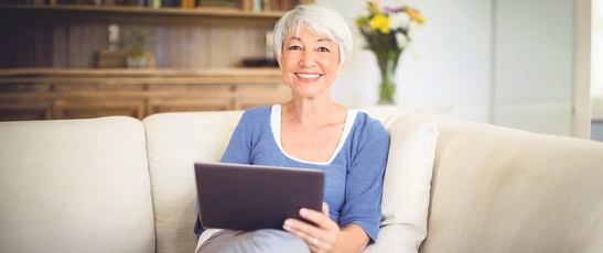 Frau sitzt auf einem Sofa und liest die digitale Tageszeitung